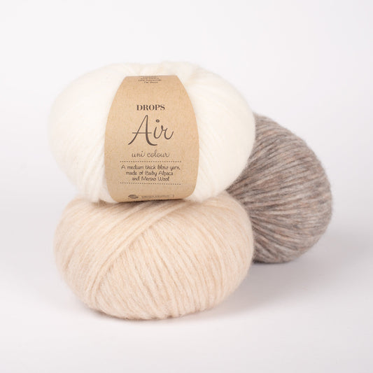 Drei Knäuel der Wolle DROPS Air in den Farben 01 natur (oben), 02 weizen (unten) und 26 beige (hinten).