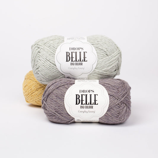 Drei Knäuel der Wolle DROPS Belle in den Farben 06 (oben, nicht mehr erhältlich), 07 zink und 04 löwenzahn (hinten).