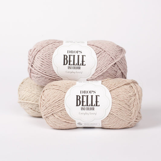 Drei Knäuel der Wolle DROPS Belle in den Farben 22 rosenwasser (oben), 23 minzcreme (vorne) und 24 sand (hinten).