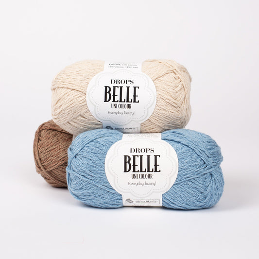 Drei Knäuel der Wolle DROPS Belle in den Farben 25 waldbraun (hinten), 03 hellbeige (oben) und 15 jeansblau (vorne).