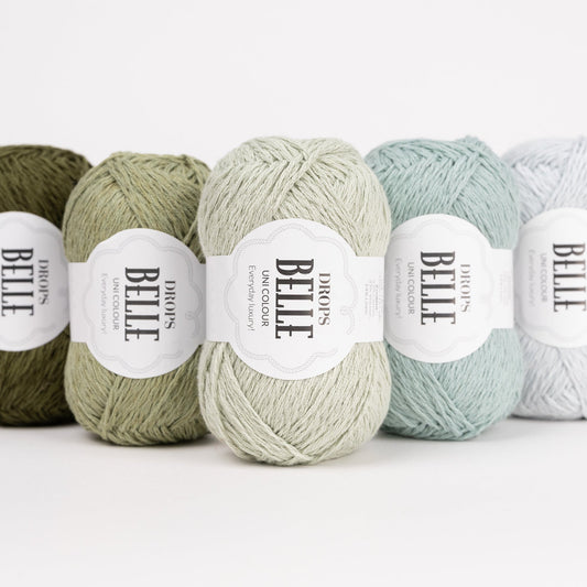 Fünf Knäuel der Wolle DROPS Belle in den Farben 38 dunkles moos, 10 moosgrün, 32 pfefferminze, 31 seegrün und 33 eiskristall (von links nach rechts).
