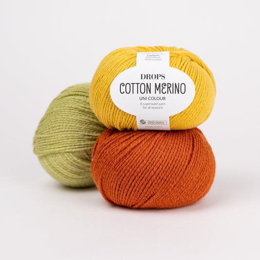 Drei Knäuel der Wolle DROPS Cotton Merino in den Farben 15 senf (oben), 25 rost (unten) und 10 pistazie (hinten).
