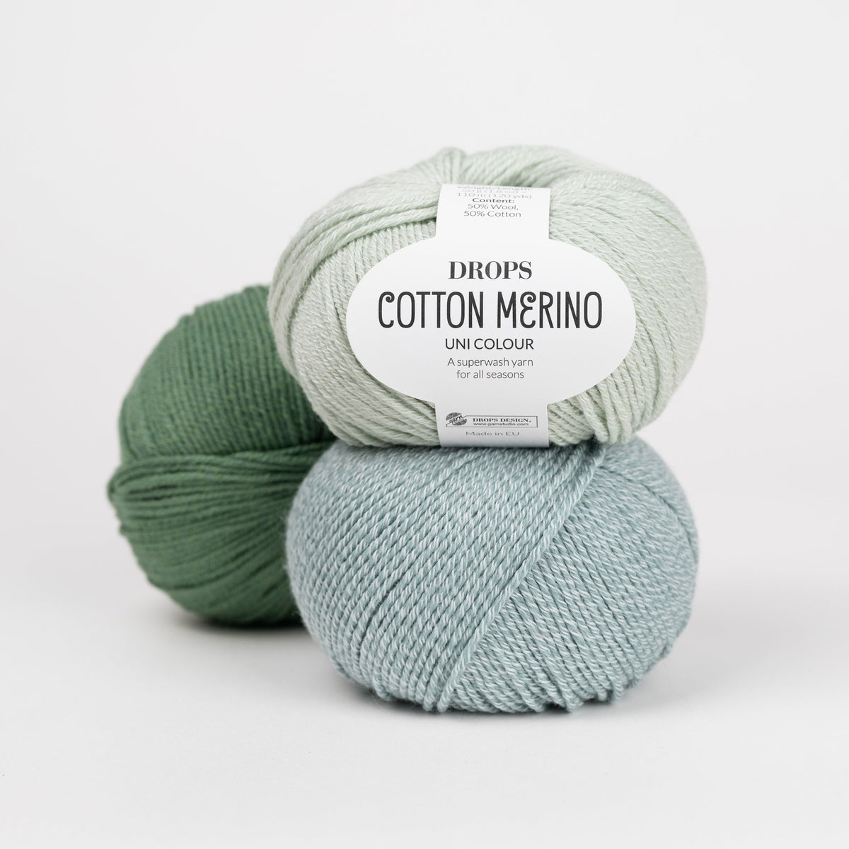 Drei Knäuel der Wolle DROPS Cotton Merino in den Farben 32 pistazieneis (oben), 29 seegrün (unten) und 11 waldgrün (hinten).