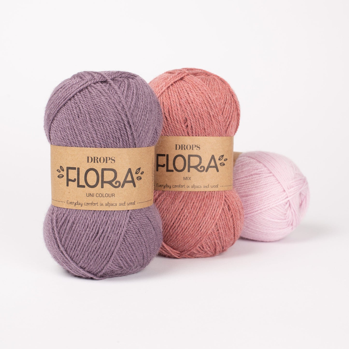 Drei Knäuel der Wolle DROPS Flora in den Farben 21 rosa, 24 erdbeerrosa und 09 amethyst (von rechts nach links).