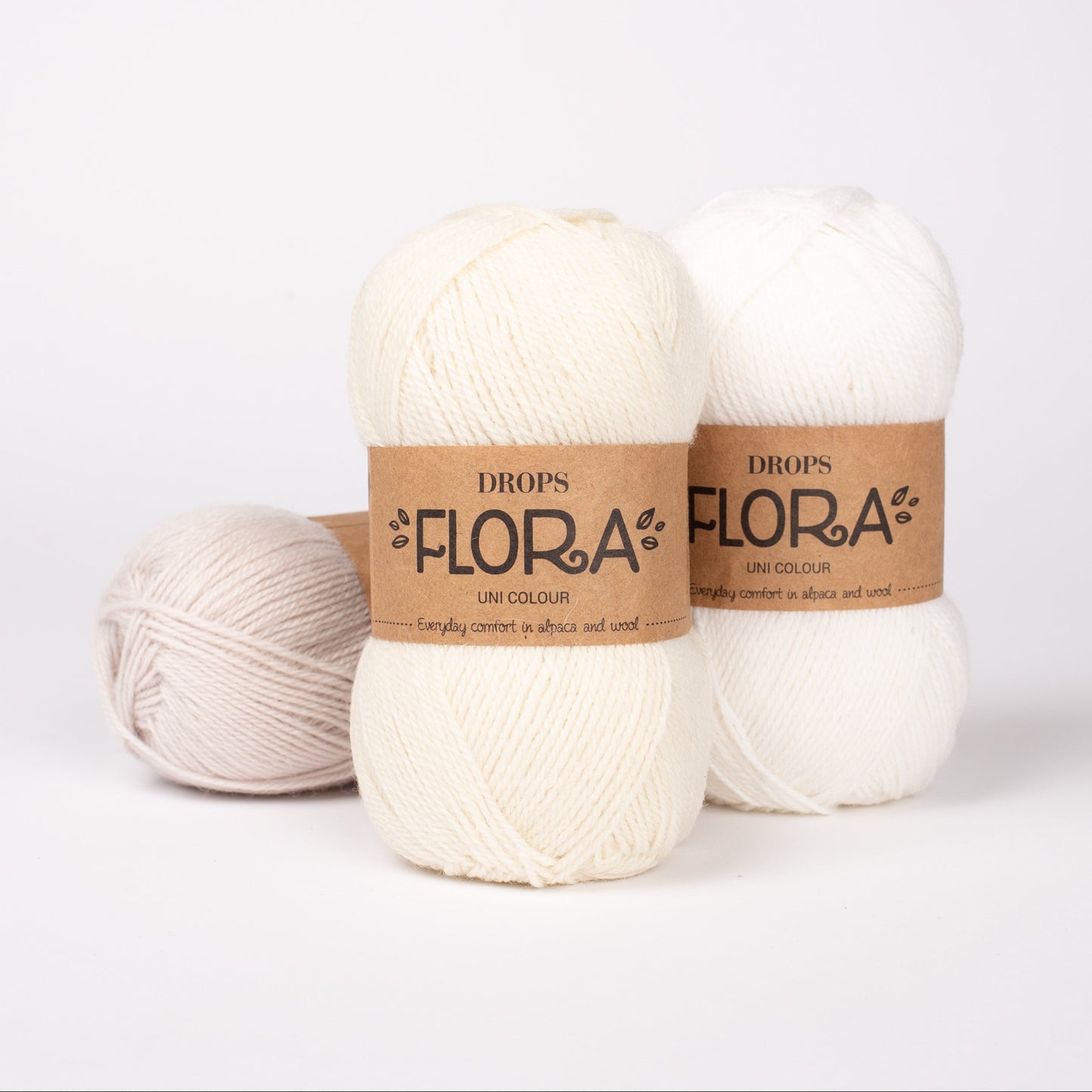 Drei Knäuel der Wolle DROPS Flora in den Farben 22 weisser nebel, 01 natur und 02 weiss (von links nach rechts).