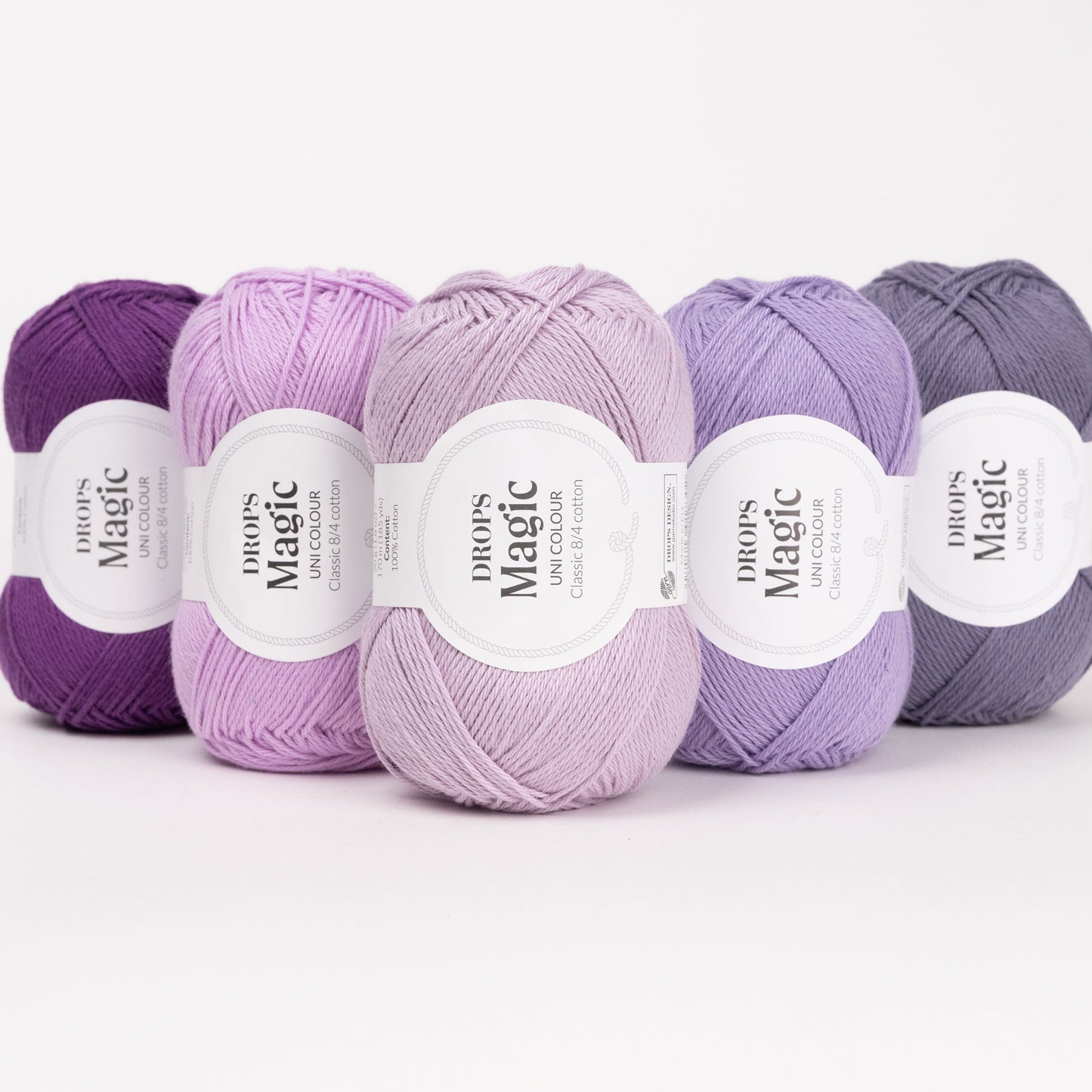 Fünf Knäuel der Wolle DROPS Magic in den Farben 11 violett, 12 orchidee, 24 eislavendel, 40 amethyst und 73 lila schatten (von links nach rechts).