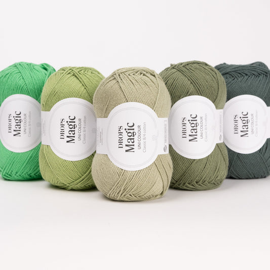 Fünf Knäuel der Wolle DROPS Magic in den Farben 46 papageigrün, 83 frühlingsblatt, 31 wildkräuter, 55 farn und 84 nebelwald (von links nach rechts).
