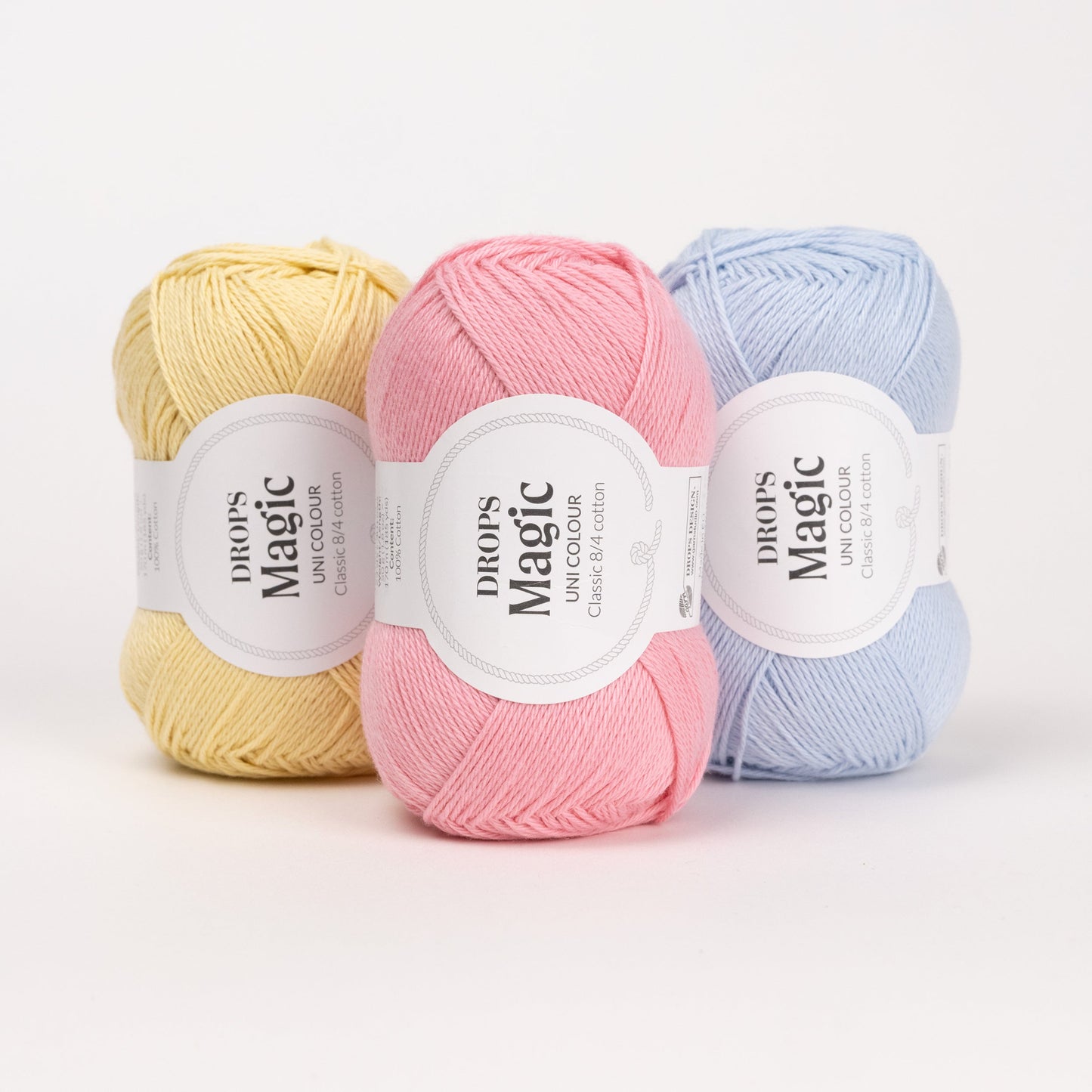 Drei Knäuel der Wolle DROPS Magic in den Farben 57 limonade, 21 pfingstrose und 26 eisblau (von links nach rechts).
