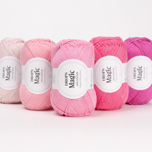 Fünf Knäuel der Wolle DROPS Magic in den Farben 69 erdbeercreme, 21 pfingstrose, 72 rosenblüte, 44 rosa flaminge und 51 magenta (von links nach rechts).