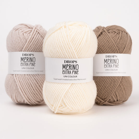 Drei Knäuel der Wolle DROPS Merino Extra Fine in den Farben 50 hellbeige, 01 natur und 51 café latte (von links nach rechts).