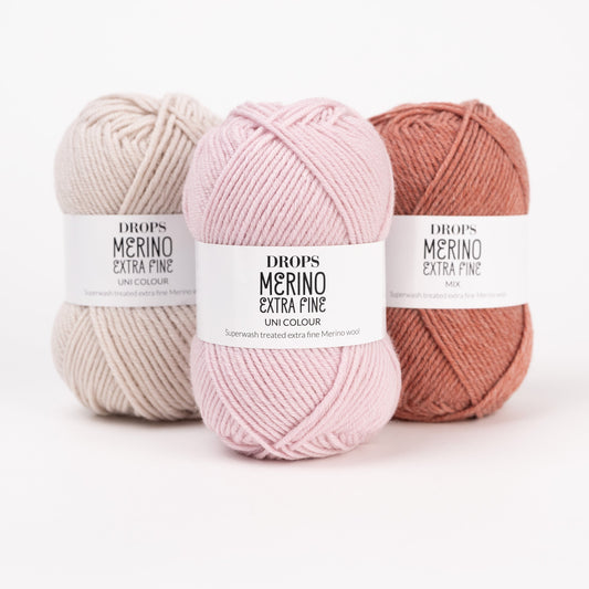 Drei Knäuel der Wolle DROPS Merino Extra Fine in den Farben 50 hellbeige, 40 puderrosa und 45 blush (von links nach rechts).