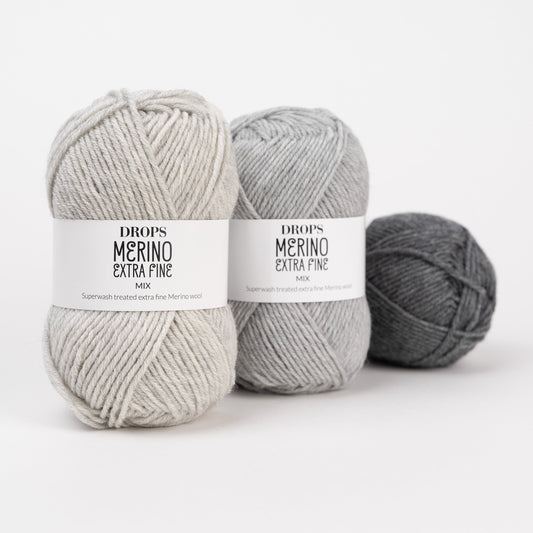 Drei Knäuel der Wolle DROPS Merino Extra Fine in den Farben 54 morgennebel, 05 hellgrau und 04 grau (von links nach rechts).