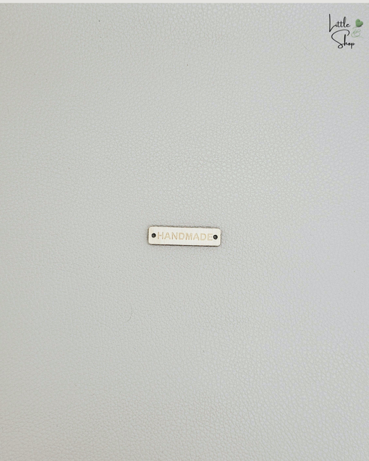 Kleines rechteckiges Label aus Holz mit dem Schriftzug "Handmade" und zwei Löchern, um es anzunähen.