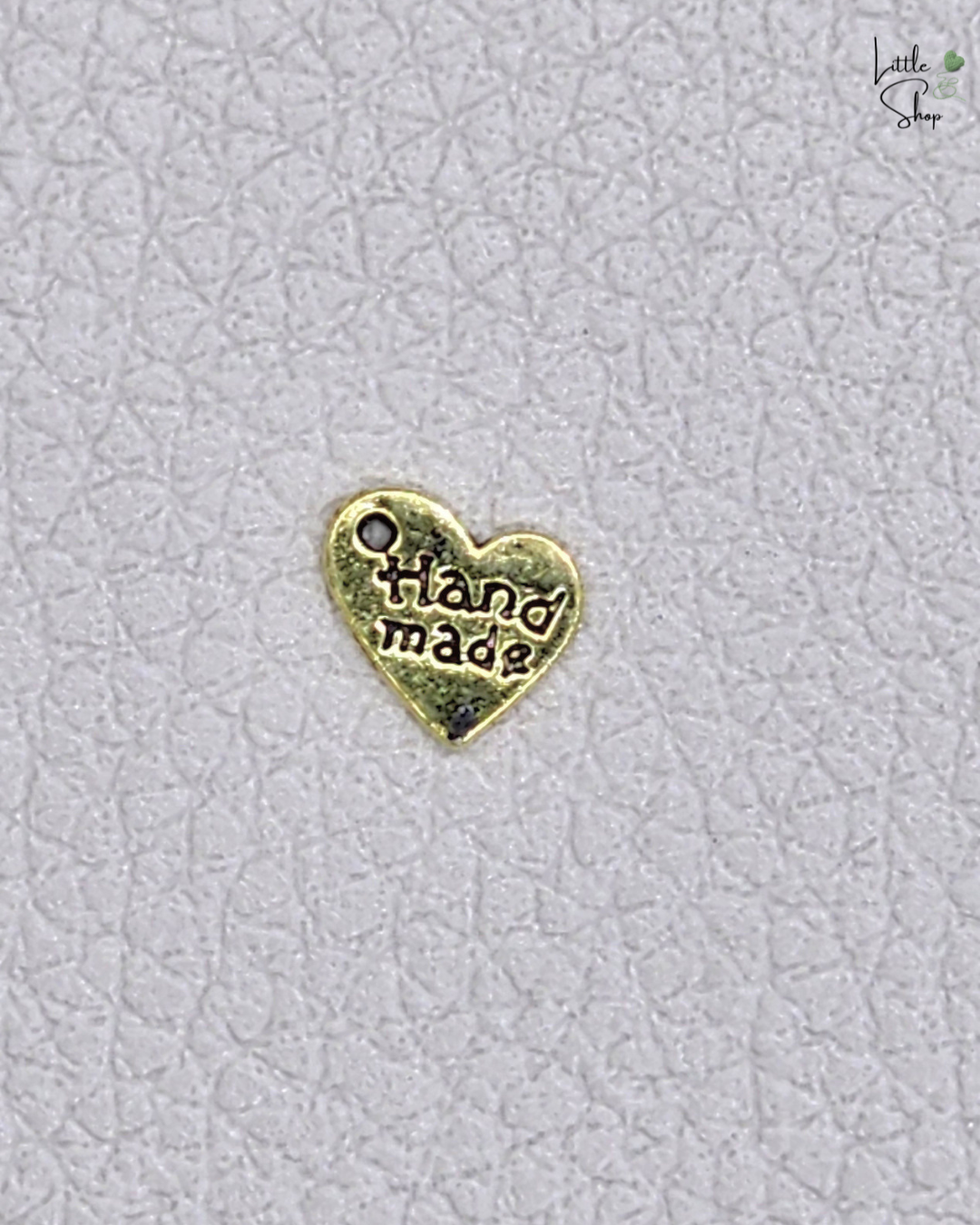 Kleines Metallabel in Herzform in antikgold mit dem Schriftzug Handmade und einer Ausstanzung, um das Label anzunähen oder aufzuhängen.