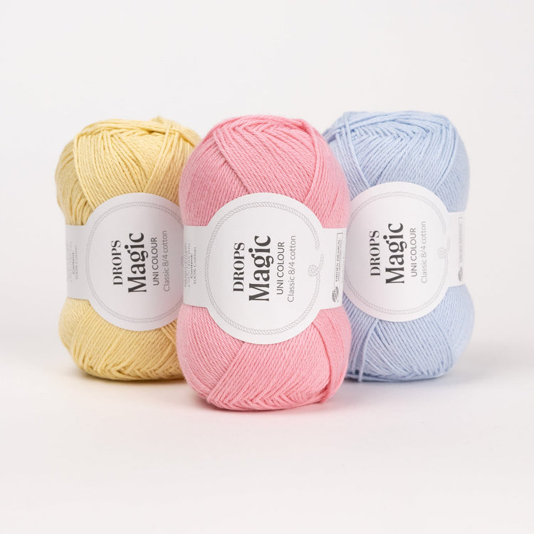 Drei Knäuel der Wolle DROPS Magic in den Farben 57 limonade, 21 pfingstrose und 26 eisblau (von links nach rechts).