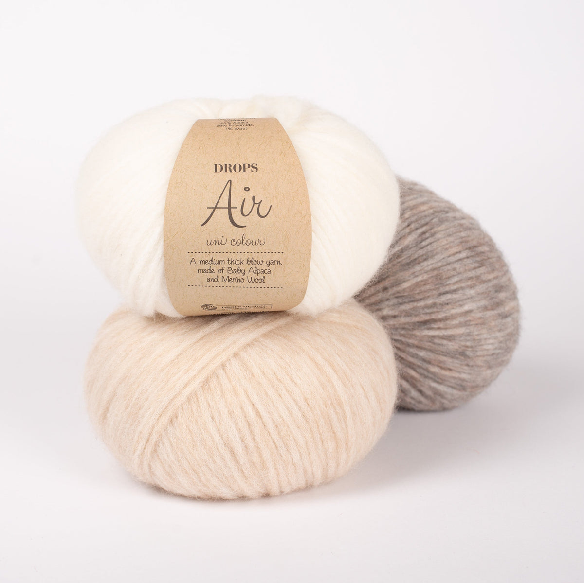 Drei Knäuel der Wolle DROPS Air in den Farben 01 natur (oben), 02 weizen (unten) und 26 beige (hinten).