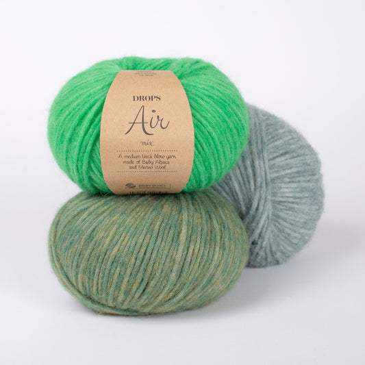 Drei Knäuel der Wolle DROPS Air in den Farben 43 papageigrün (oben), 12 moosgrün (unten) und 30 salbeigrün (hinten).