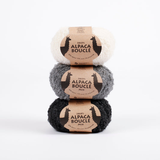 Drei Knäuel der Wolle DROPS Alpaca Bouclé in den Farben 0100 natur, 0517 grau und 0506 (von oben nach unten - die Farbe 0506 ist nicht mehr erhältlich).