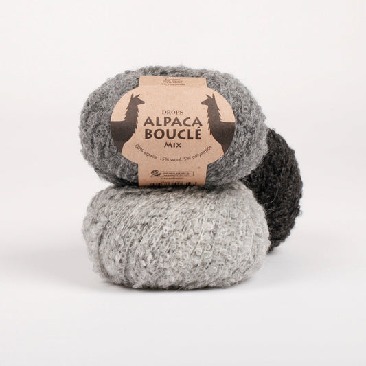 Drei Knäuel der Wolle DROPS Alpaca Bouclé in den Farben 0517 grau (oben), 5110 hellgrau (unten) und 0506 (hinten - nicht mehr erhältlich).