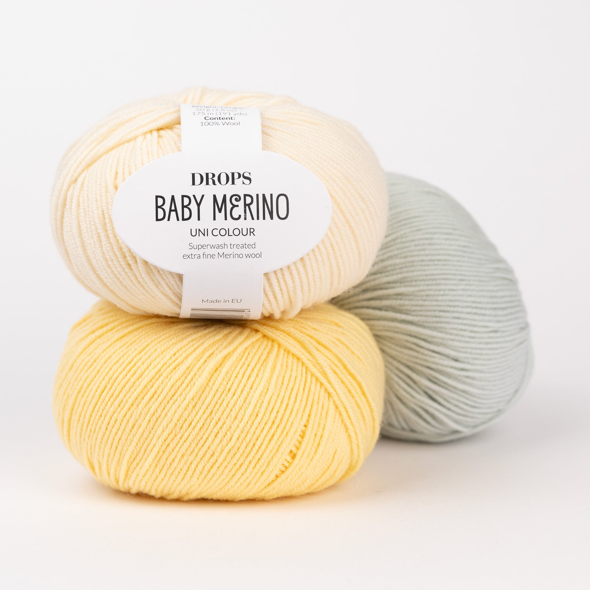 Drei Knäuel der Wolle DROPS Baby Merino in den Farben 03 hellgelb, 04 gelb und 58 pistazieneis (von links oben über links unten nach rechts).