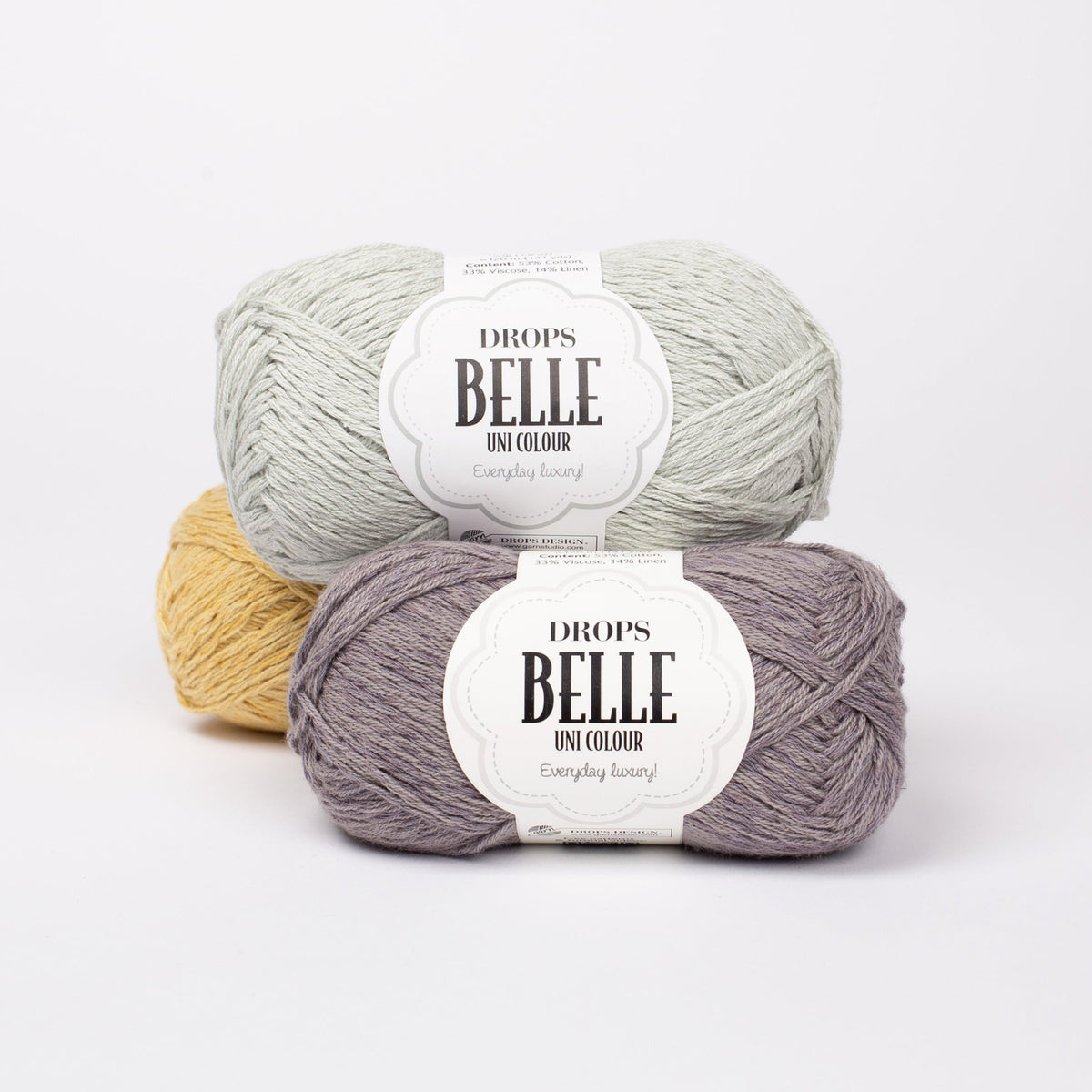 Drei Knäuel der Wolle DROPS Belle in den Farben 06 (oben, nicht mehr erhältlich), 07 zink und 04 löwenzahn (hinten).