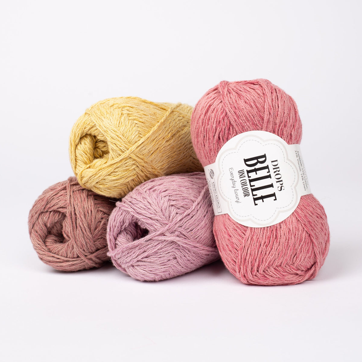 Vier Knäuel der Wolle DROPS Belle in den Farben 21 rosenmandel (links unten), 16 mauve (Mitten unten), 04 löwenzahn (links oben) und 11 altrosa (rechts).