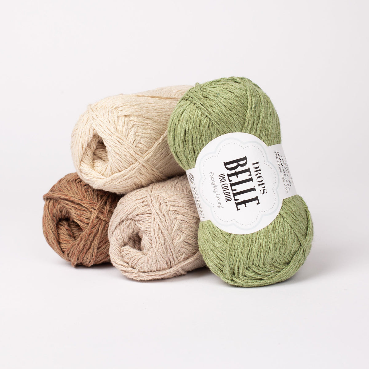 Vier Knäuel der Wolle DROPS Belle in den Farben 25 waldbraun (links unten), 02  natur (links oben), 03 hellbeige (Mitte) und 10 moosgrün (rechts).