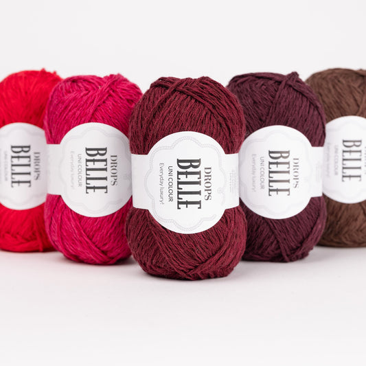 Fünf Knäuel der Wolle DROPS Belle in den Farben 29 rot, 12 kirsche, 36 rubinrot, 40 pflaumenwein und 39 schokolade (von links nach rechts). 