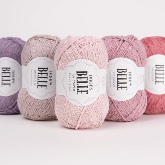 Fünf Knäuel der Wolle DROPS Belle in den Farben 34 lila orcchidee, 22 rosenwasser, 30 puderrosa, 16 mauve und 11 altrosa (von links nach rechts).