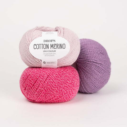 Drei Knäuel der Wolle DROPS Cotton Merino in den Farben 05 puderrosa (oben), 36 himbeersorbet (unten) und 23 lavendel (hinten).