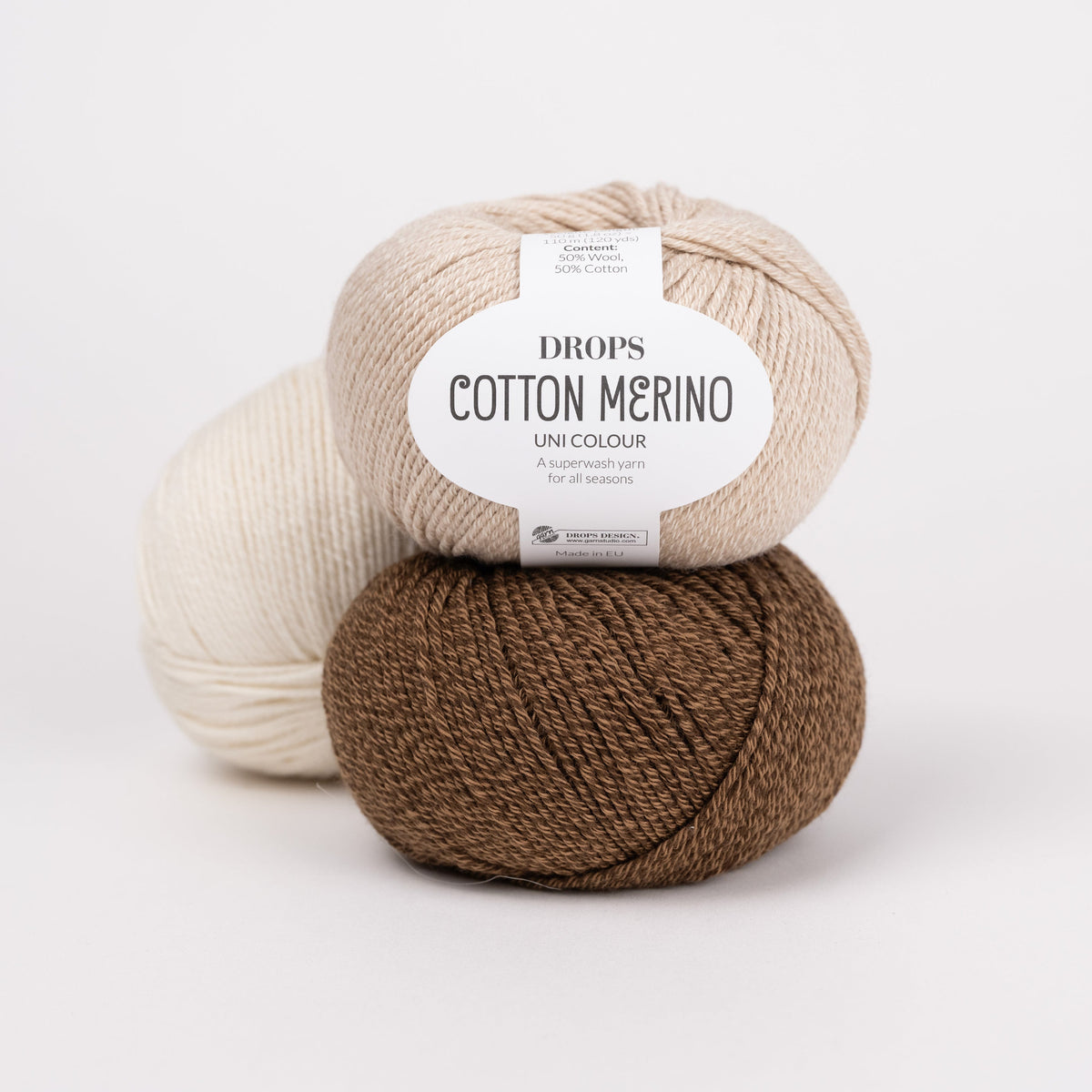 Drei Knäuel der Wolle DROPS Cotton Merino in den Farben 38 weizen (oben), 39 pecan pie (unten) und 01 natur (hinten).