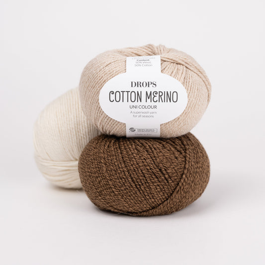 Drei Knäuel der Wolle DROPS Cotton Merino in den Farben 38 weizen (oben), 39 pecan pie (unten) und 01 natur (hinten).