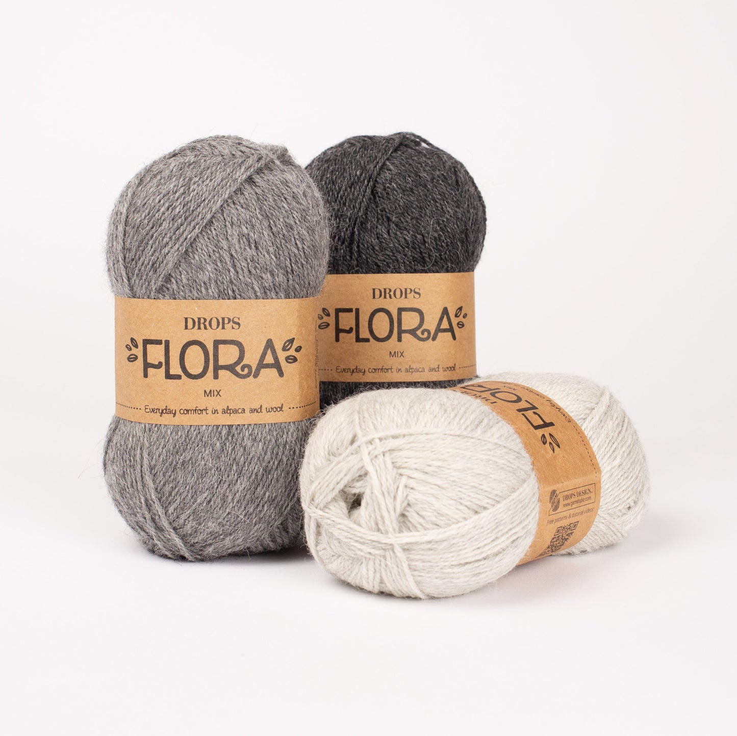 Drei Knäuel der Wolle DROPS Flora in den Farben 04 mittelgrau, 05 dunkelgrau und 03 hellgrau (von links nach rechts).