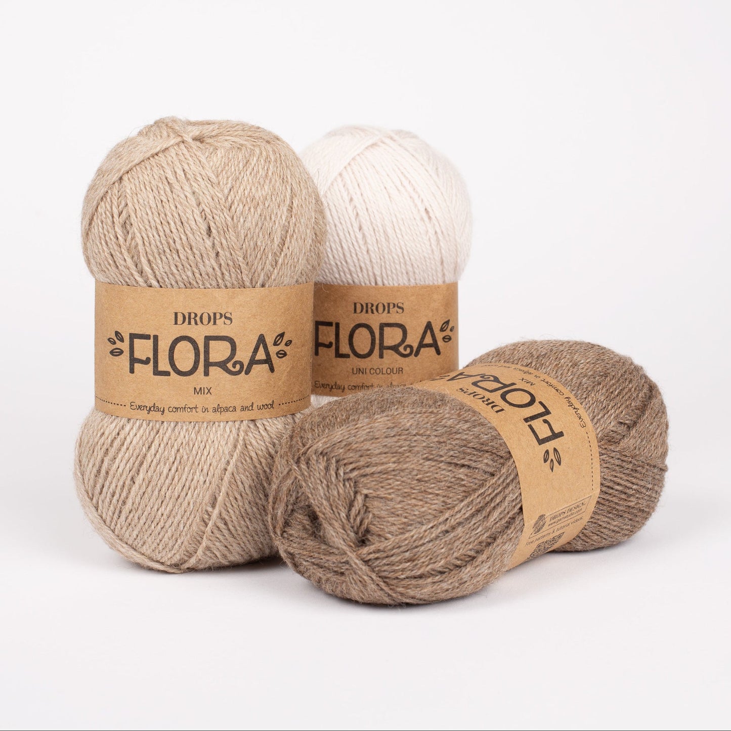 Drei Knäuel der Wolle DROPS Flora in den Farben 07 beige, 08 braun und 22 weisser nebel (links, rechts, Mitte).