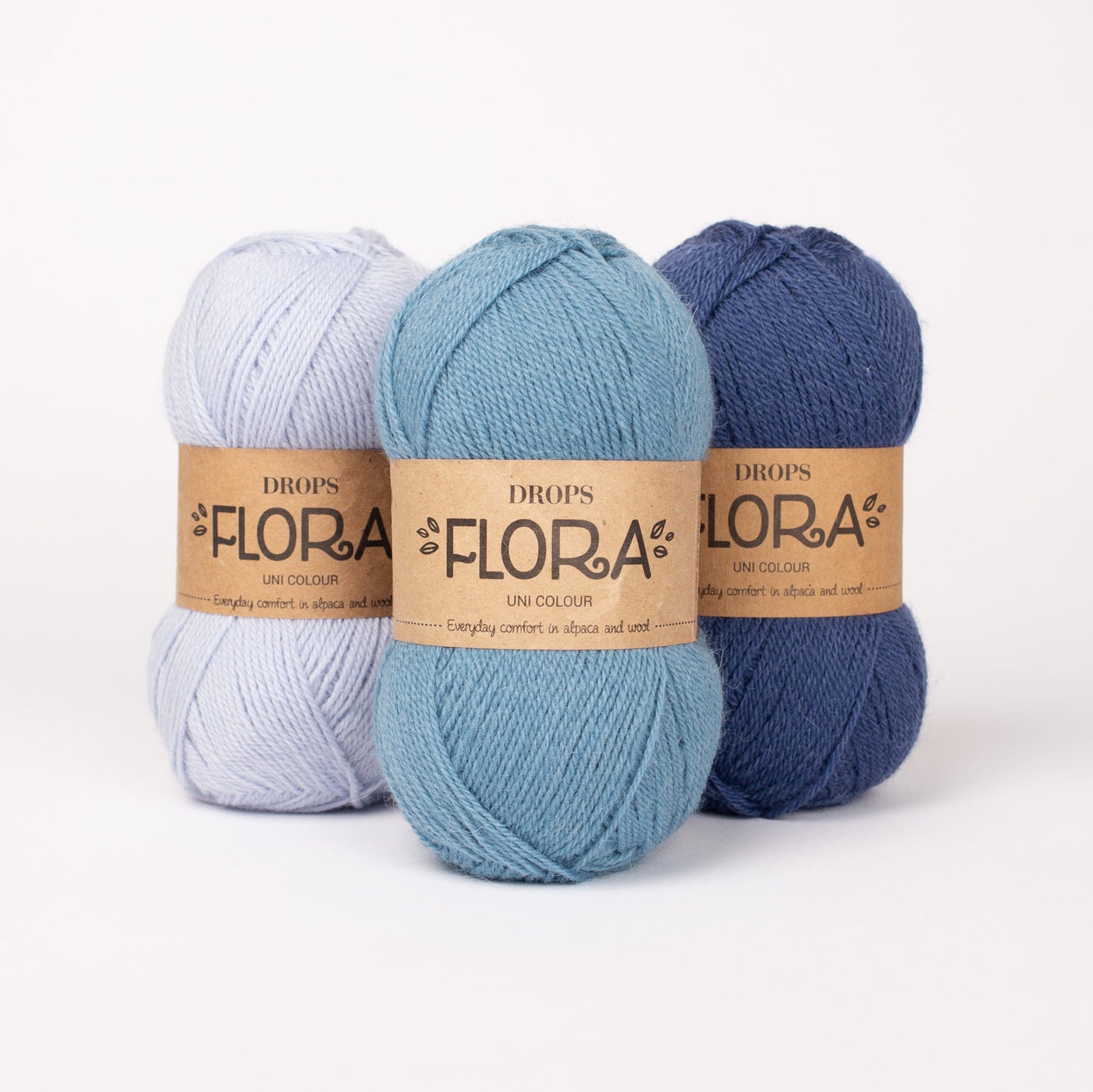 Drei Knäuel der Wolle DROPS Flora in den Farben 14 eisblau, 13 jeansblau und 10 indigo (von links nach rechts).