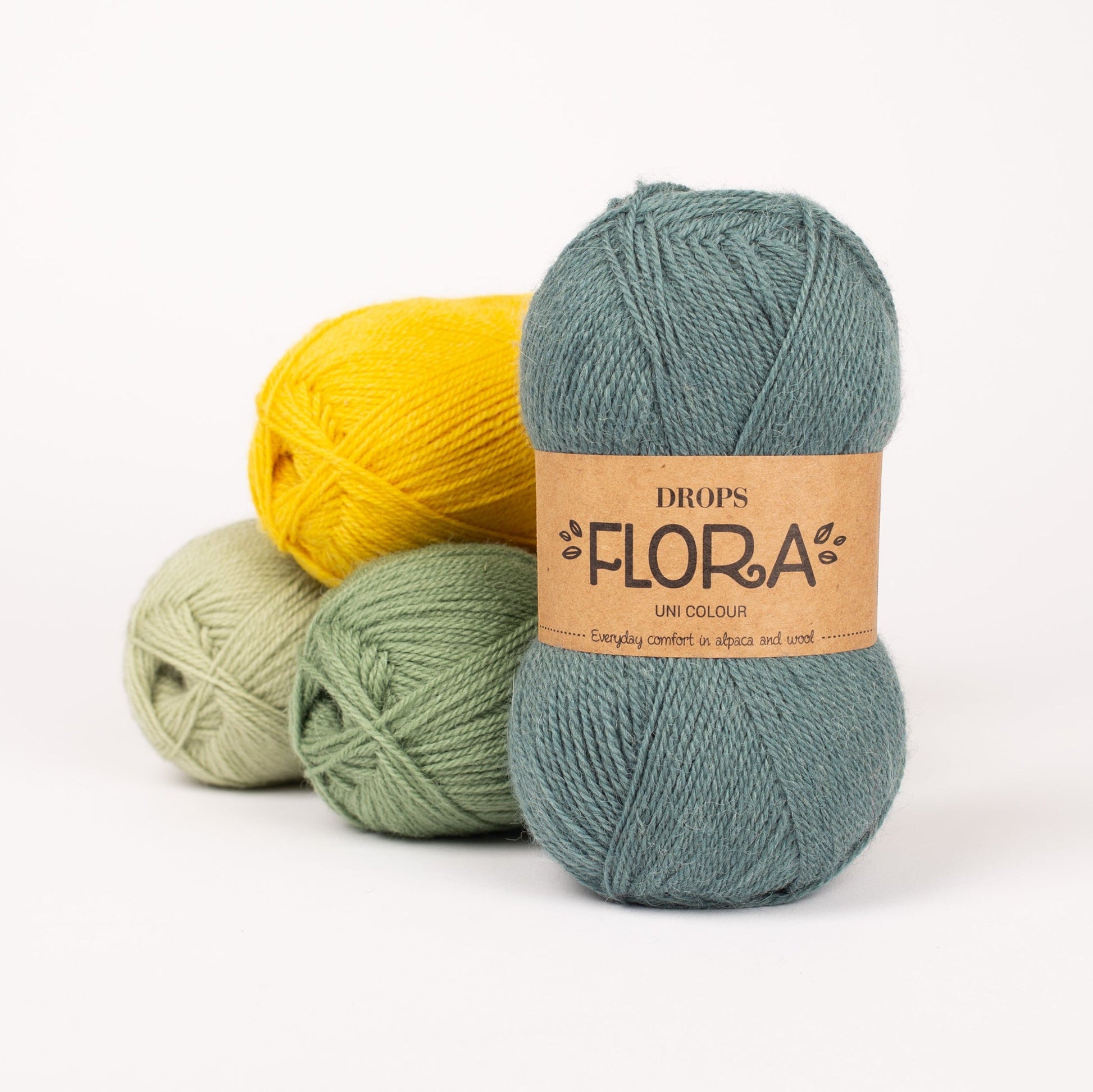 Vier Knäuel der Wolle DROPS Flora in den Farben 16 pistazie, 15 grün, 17 gelb und 23 nebelwald (von links nach rechts).