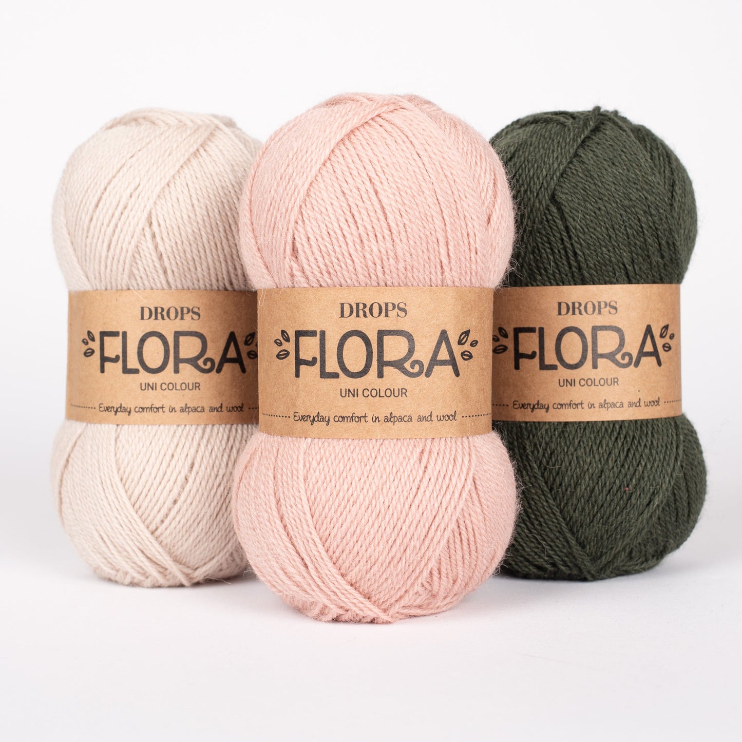 Drei Knäuel der Wolle DROPS Flora in den Farben 30 wüstenrose, 31 sand und 32 dunkelgrün (von links nach rechts).