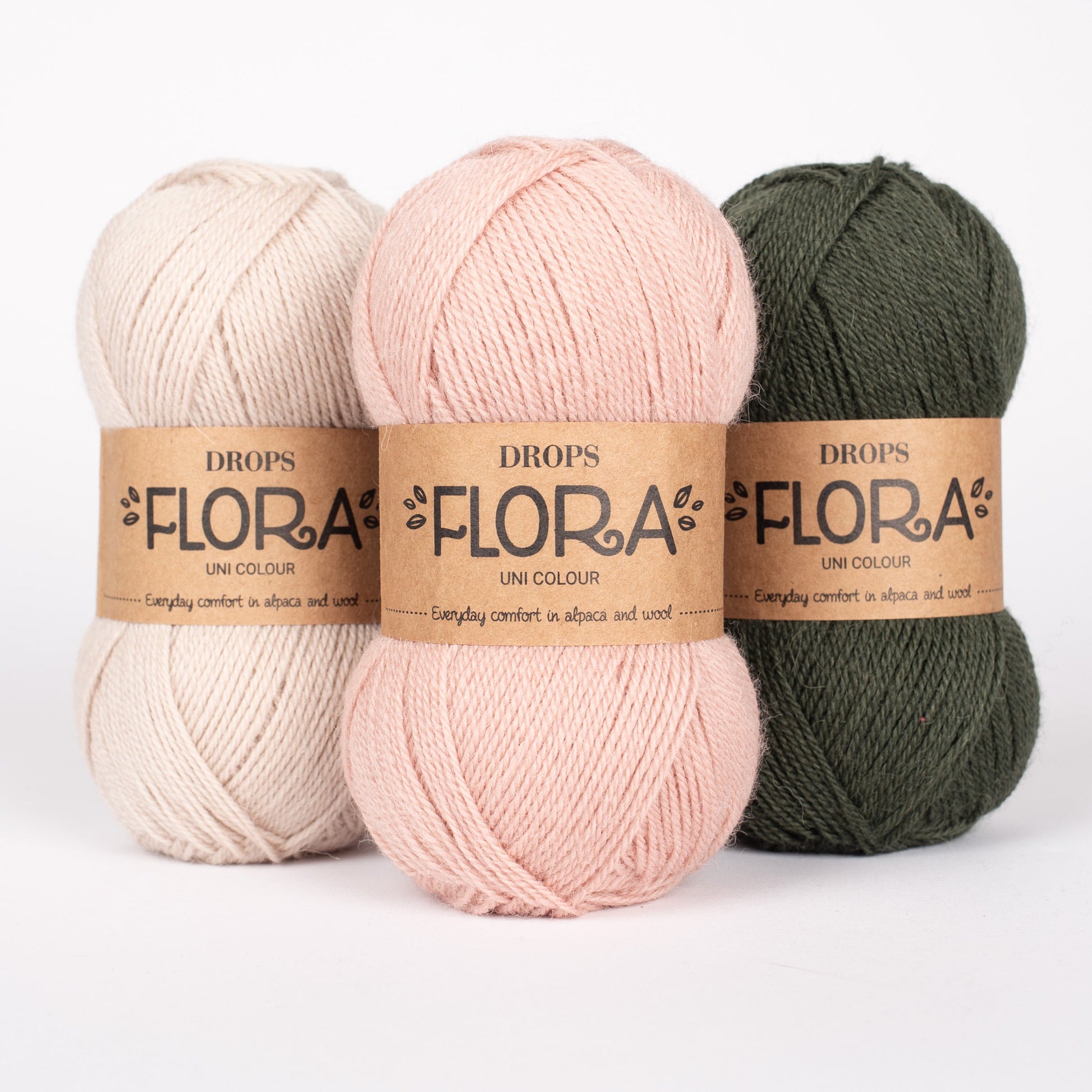 Drei Knäuel der Wolle DROPS Flora in den Farben 30 wüstenrose, 31 sand und 32 dunkelgrün (von links nach rechts).