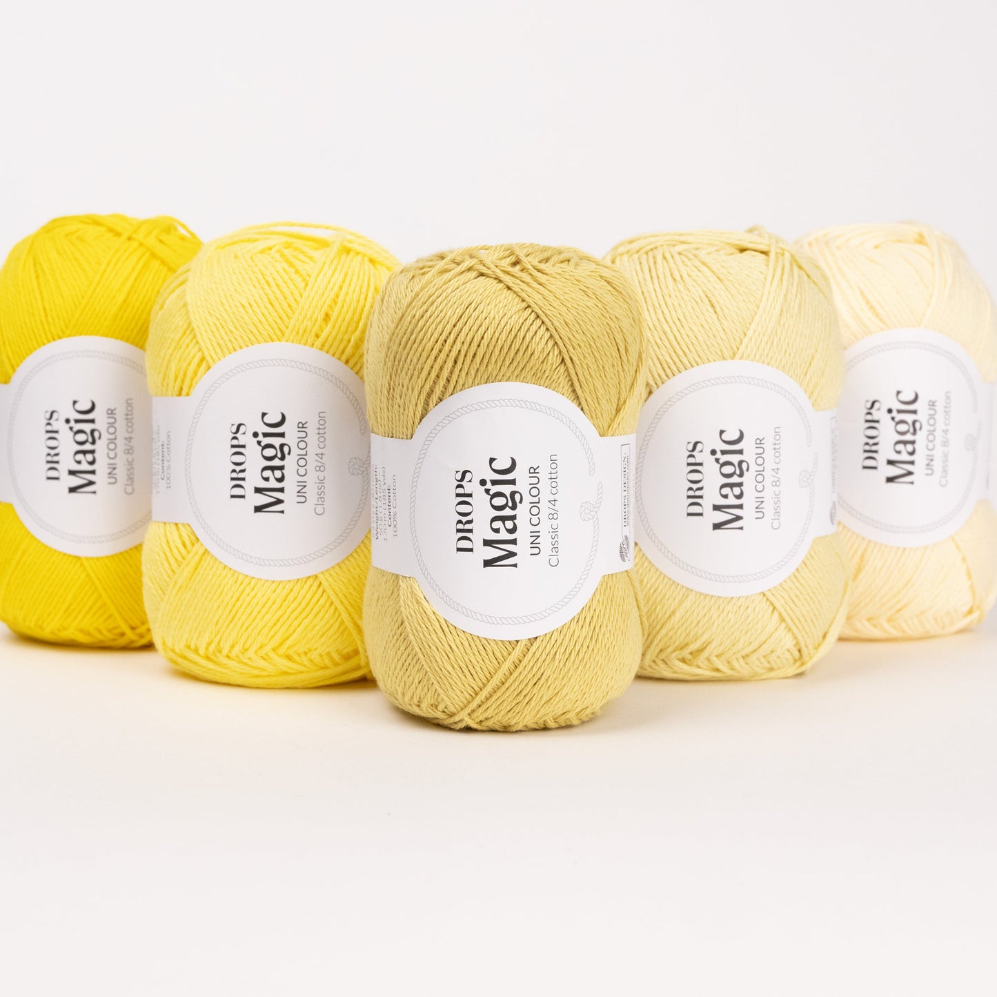 Fünf Knäuel der Wolle DROPS Magic in den Farben 09 gelb, 65 kanariengelb, 64 löwenzahn, 57 limonade und 08 vanille (von links nach rechts).