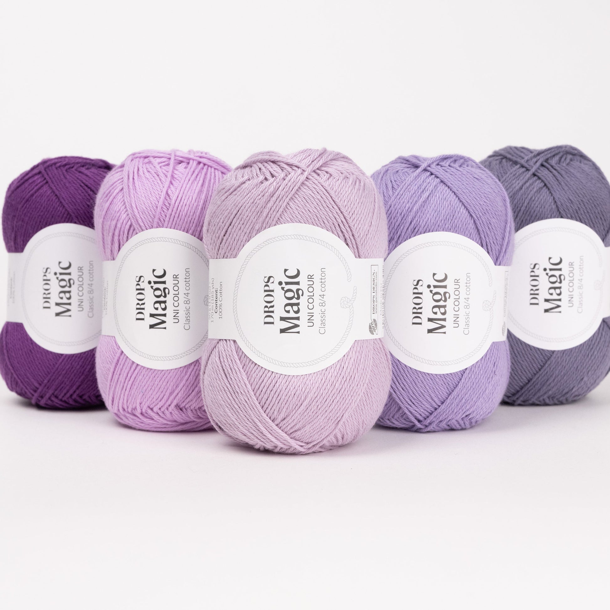 Fünf Knäuel der Wolle DROPS Magic in den Farben 11 violett, 12 orchidee, 24 eislavendel, 40 amethyst und 73 lila schatten (von links nach rechts).