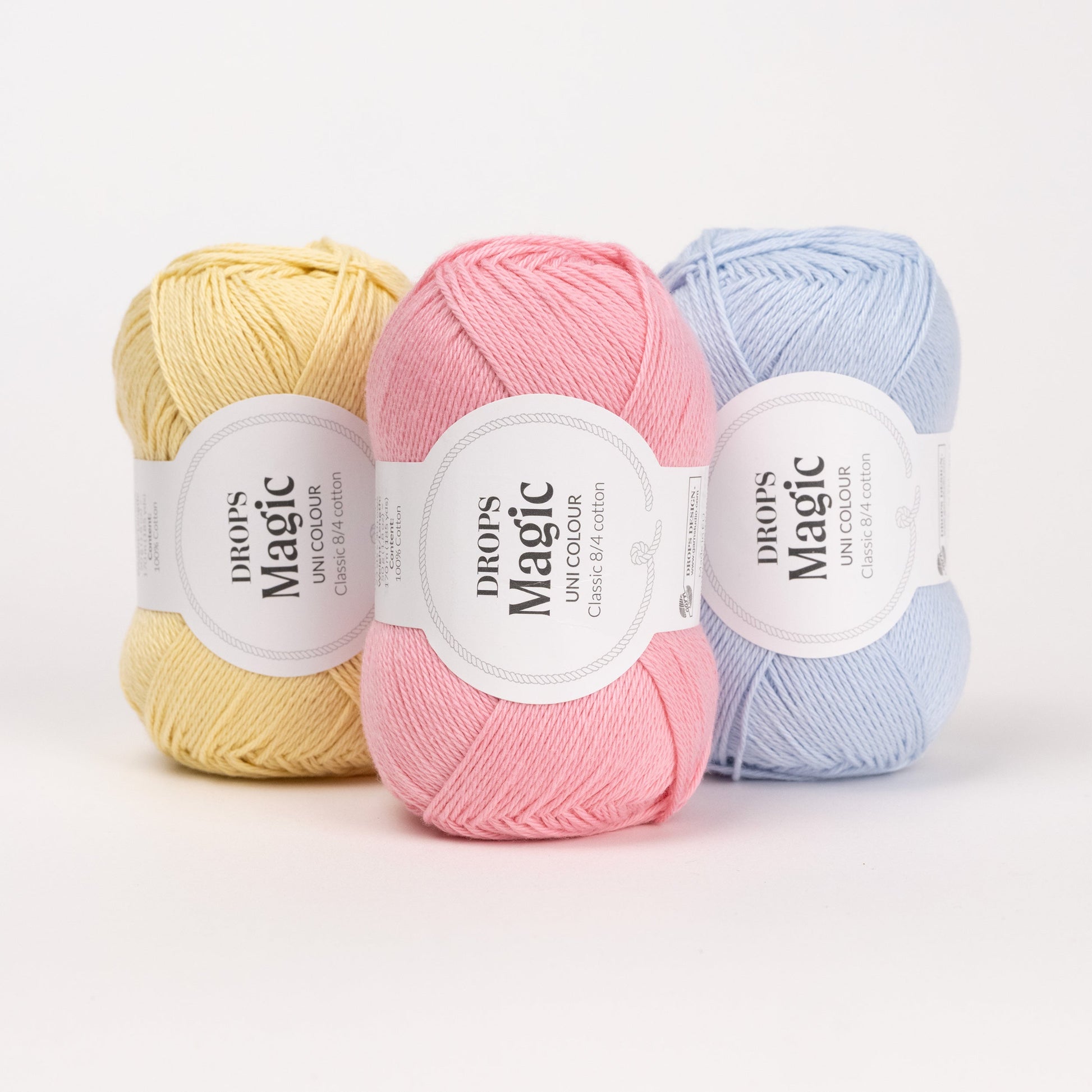 Drei Knäuel der Wolle DROPS Magic in den Farben 57 limonade, 21 pfingstrose und 26 eisblau (von links nach rechts).