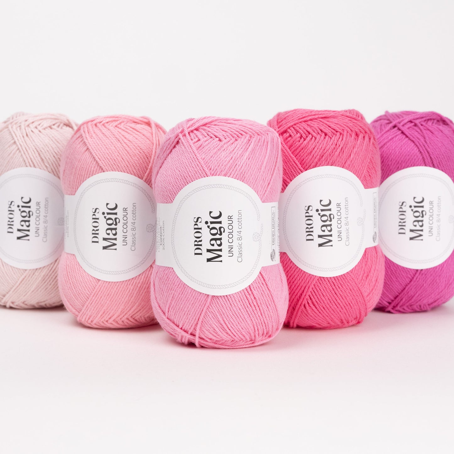 Fünf Knäuel der Wolle DROPS Magic in den Farben 69 erdbeercreme, 21 pfingstrose, 72 rosenblüte, 44 rosa flaminge und 51 magenta (von links nach rechts).
