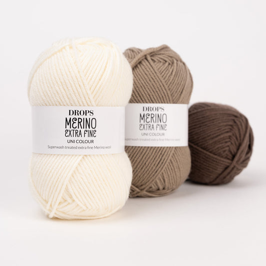 Drei Knäuel der Wolle DROPS Merino Extra Fine in den Farben 01 natur, 51 café latte und 49 schokolade (von links nach rechts).