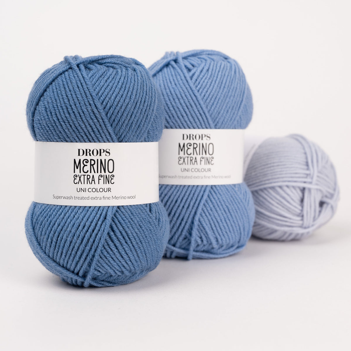 Drei Knäuel der Wolle DROPS Merino Extra Fine in den Farben 23 graublau, 19 hellblau und 39 eisblau (von links nach rechts).
