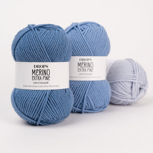 Drei Knäuel der Wolle DROPS Merino Extra Fine in den Farben 23 graublau, 19 hellblau und 39 eisblau (von links nach rechts).