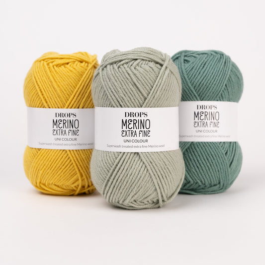 Drei Knäuel der Wolle DROPS Merino Extra Fine in den Farben 30 senf, 31 pistazie und 31 waldgrün (von links nach rechts).