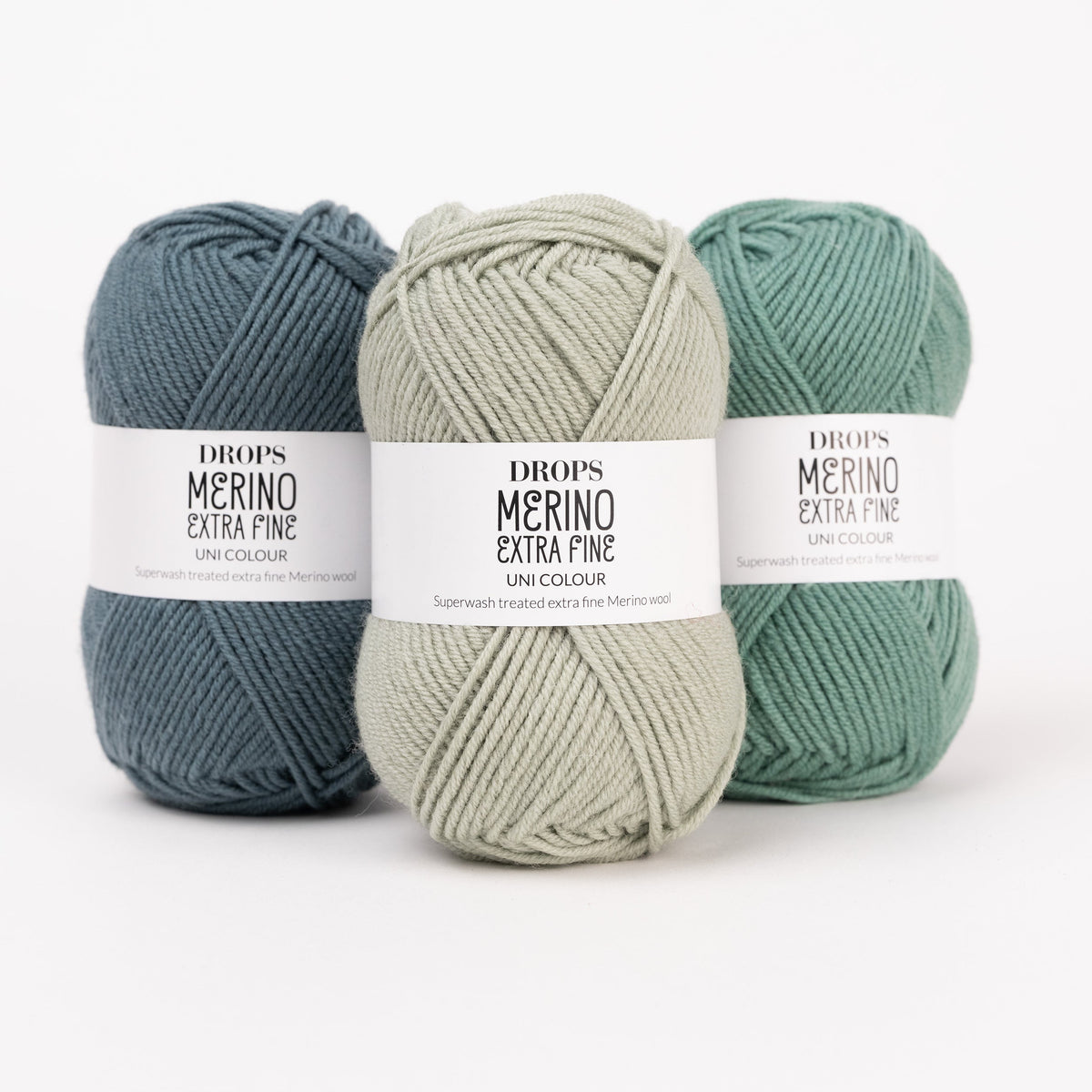 Drei Knäuel der Wolle DROPS Merino Extra Fine in den Farben 37 nebelwald, 26 pistazie und 31 waldgrün (von links nach rechts).