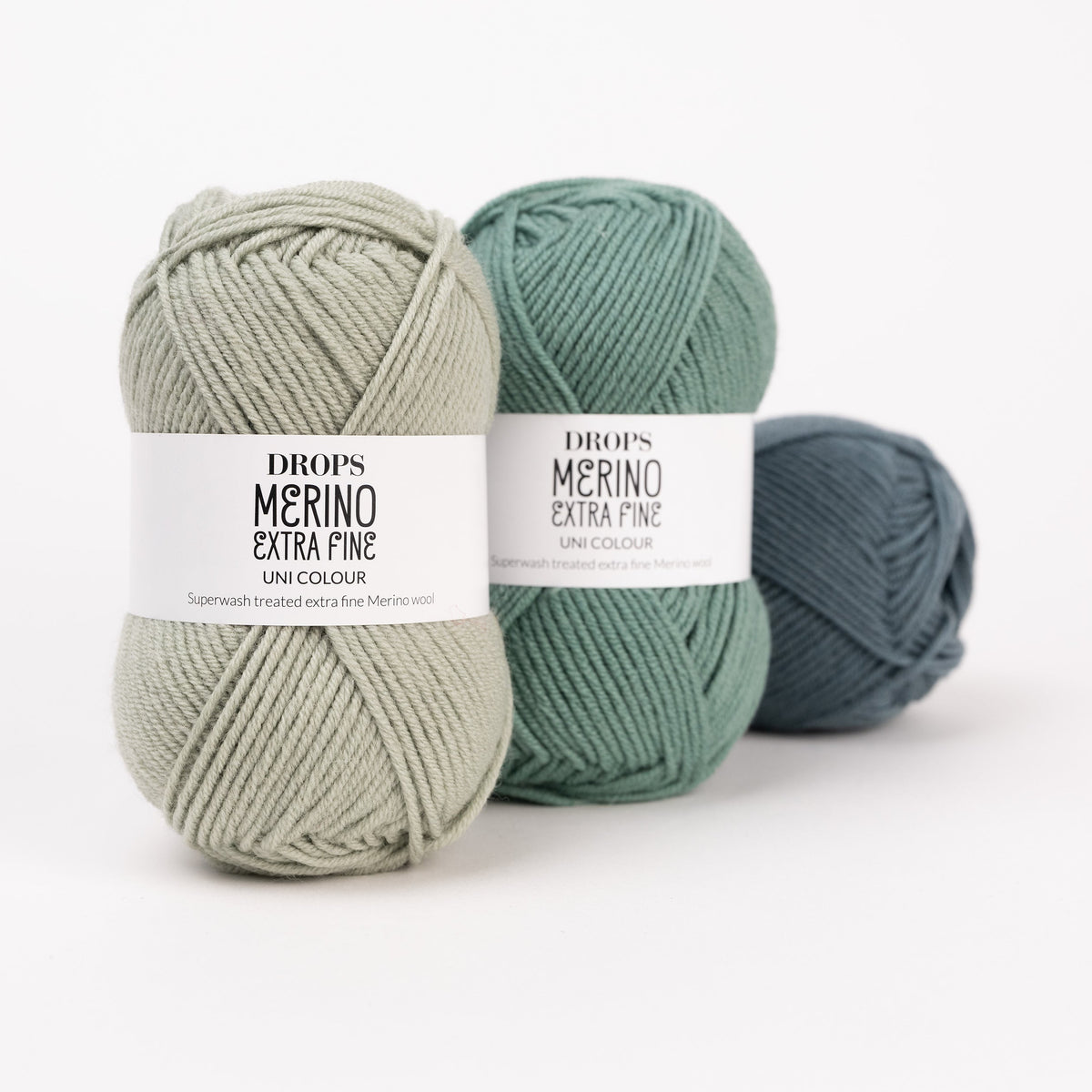 Drei Knäuel der Wolle DROPS Merino Extra Fine in den Farben 37 nebelwald, 31 waldgrün und 26 pistazie (von rechts nach links).