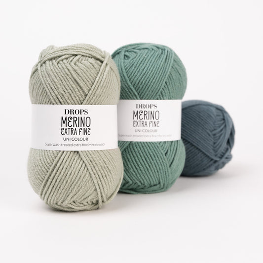 Drei Knäuel der Wolle DROPS Merino Extra Fine in den Farben 37 nebelwald, 31 waldgrün und 26 pistazie (von rechts nach links).