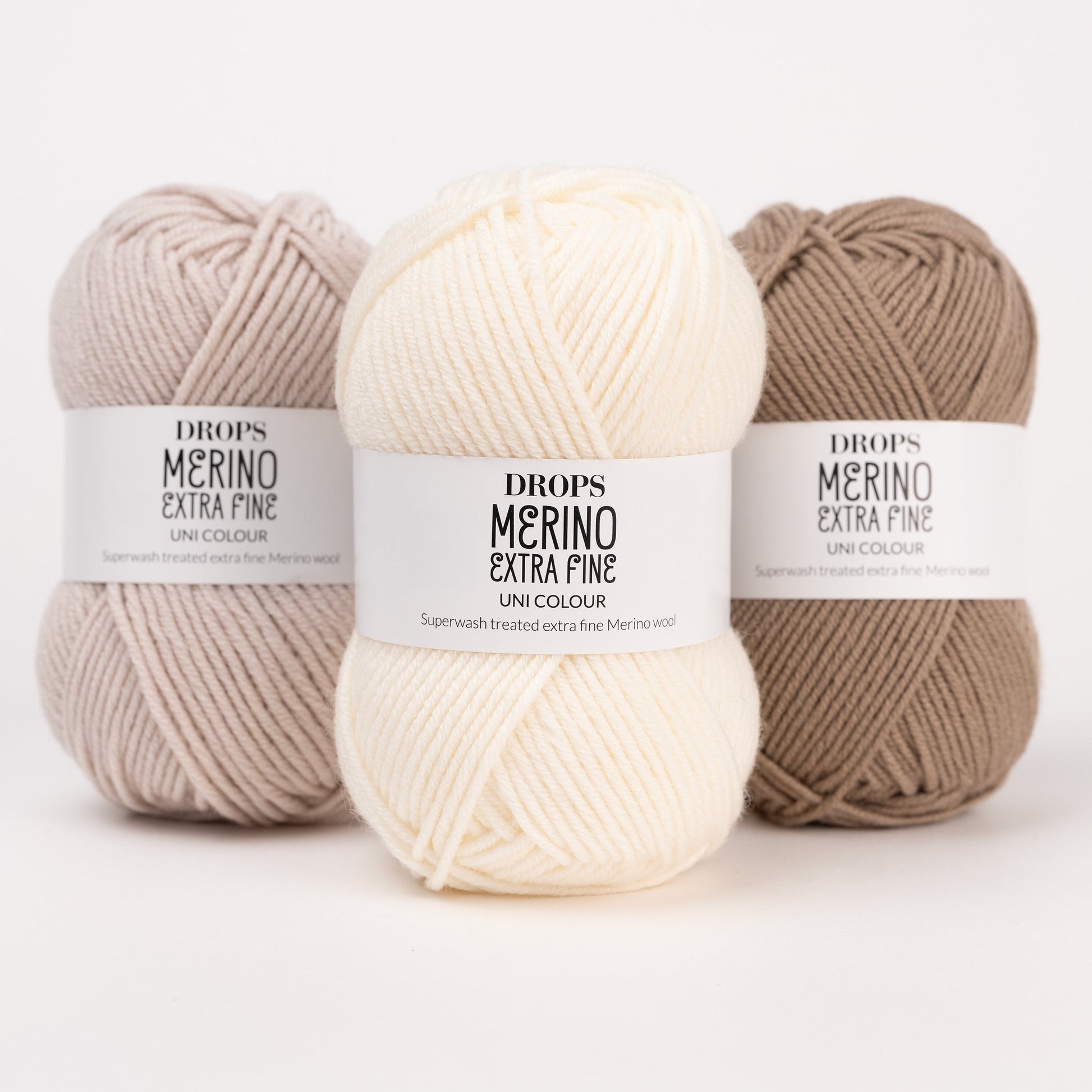 Drei Knäuel der Wolle DROPS Merino Extra Fine in den Farben 50 hellbeige, 01 natur und 51 café latte (von links nach rechts).